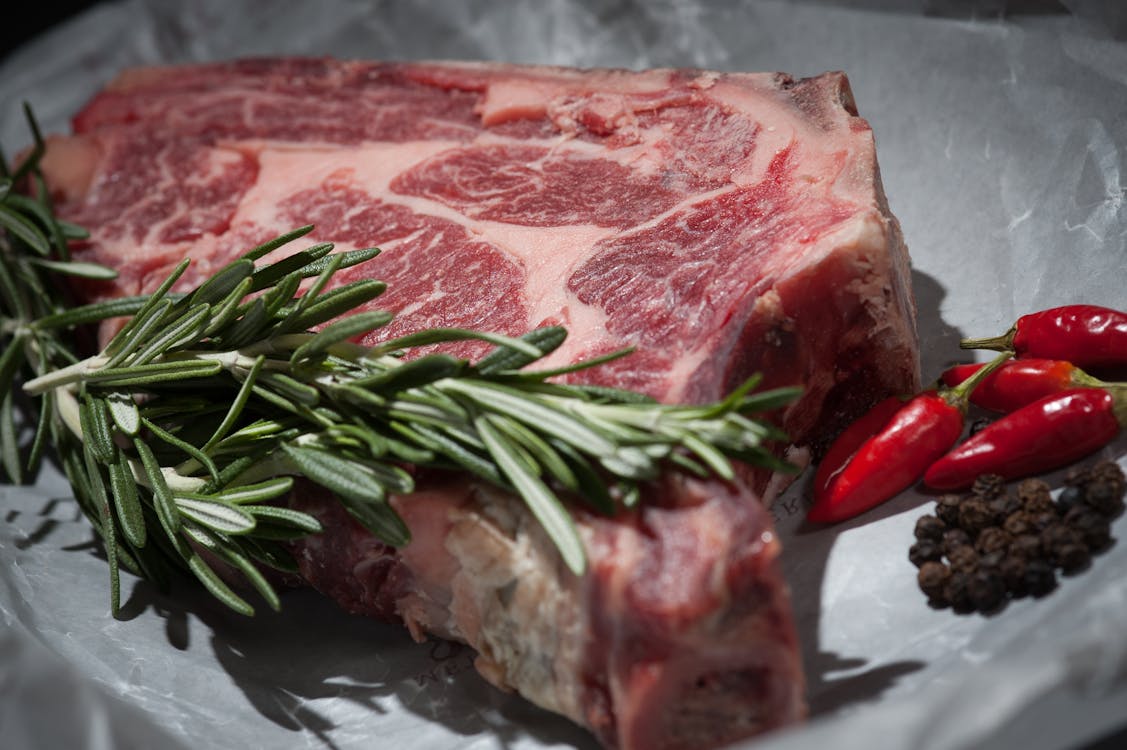 Corte de carne vermelha fresca acompanhada de alecrim e pimentas, destacando fontes ricas em proteína para uma dieta equilibrada.