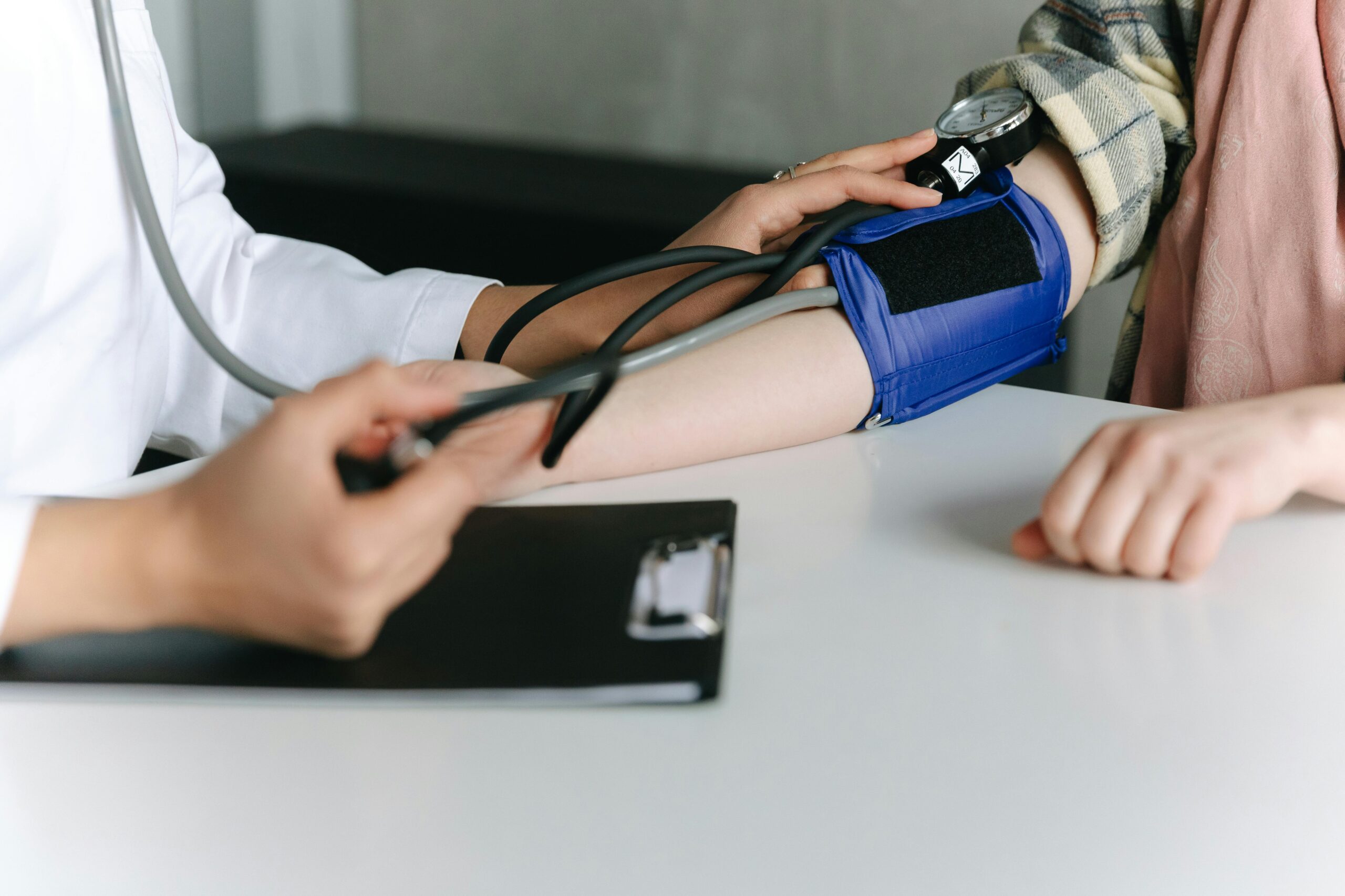 Profissional de saúde usando esfigmomanômetro digital azul para medir pressão arterial de paciente em consultório médico