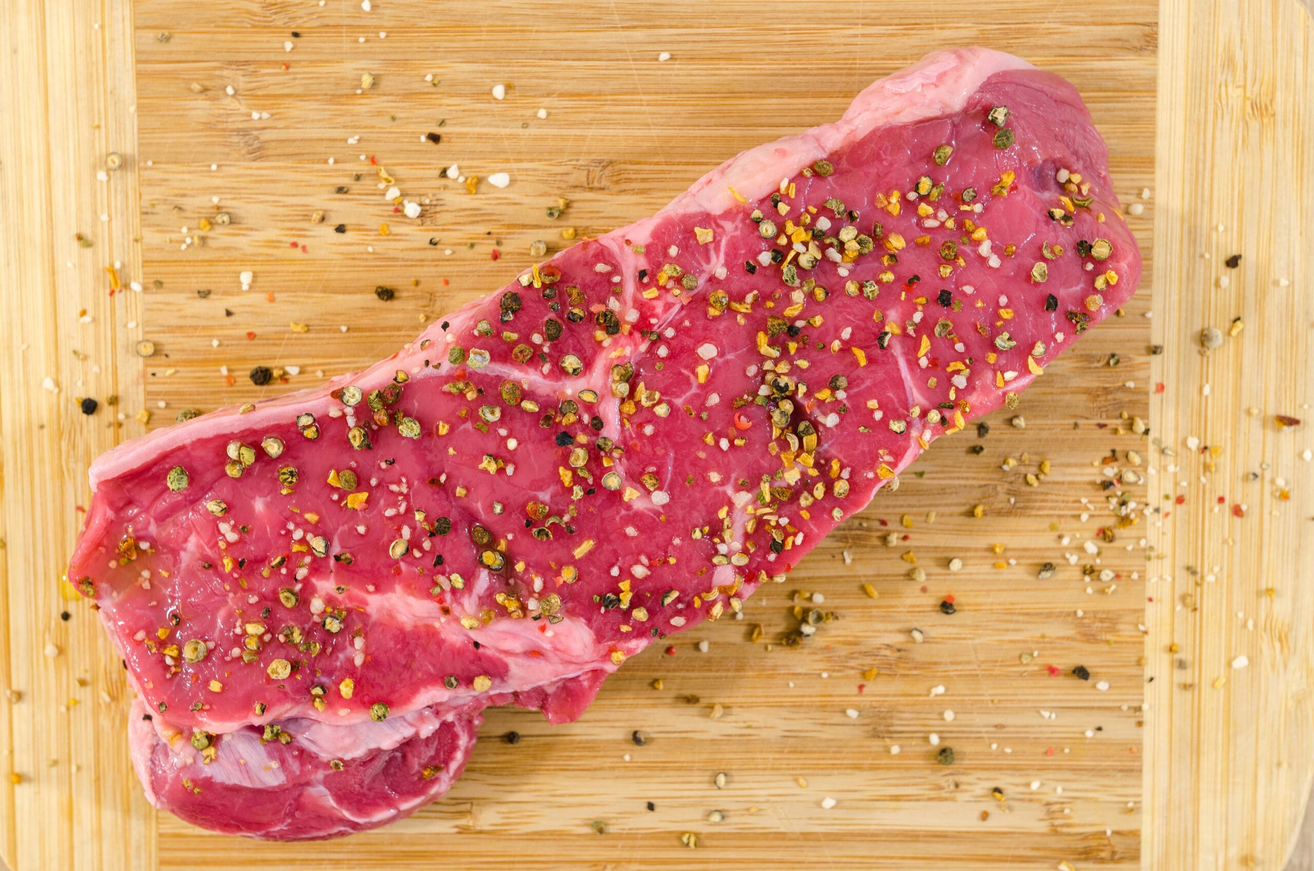 Carne vermelha crua temperada com especiarias e sal grosso sobre tábua de madeira, representando alimentos da dieta cetogênica