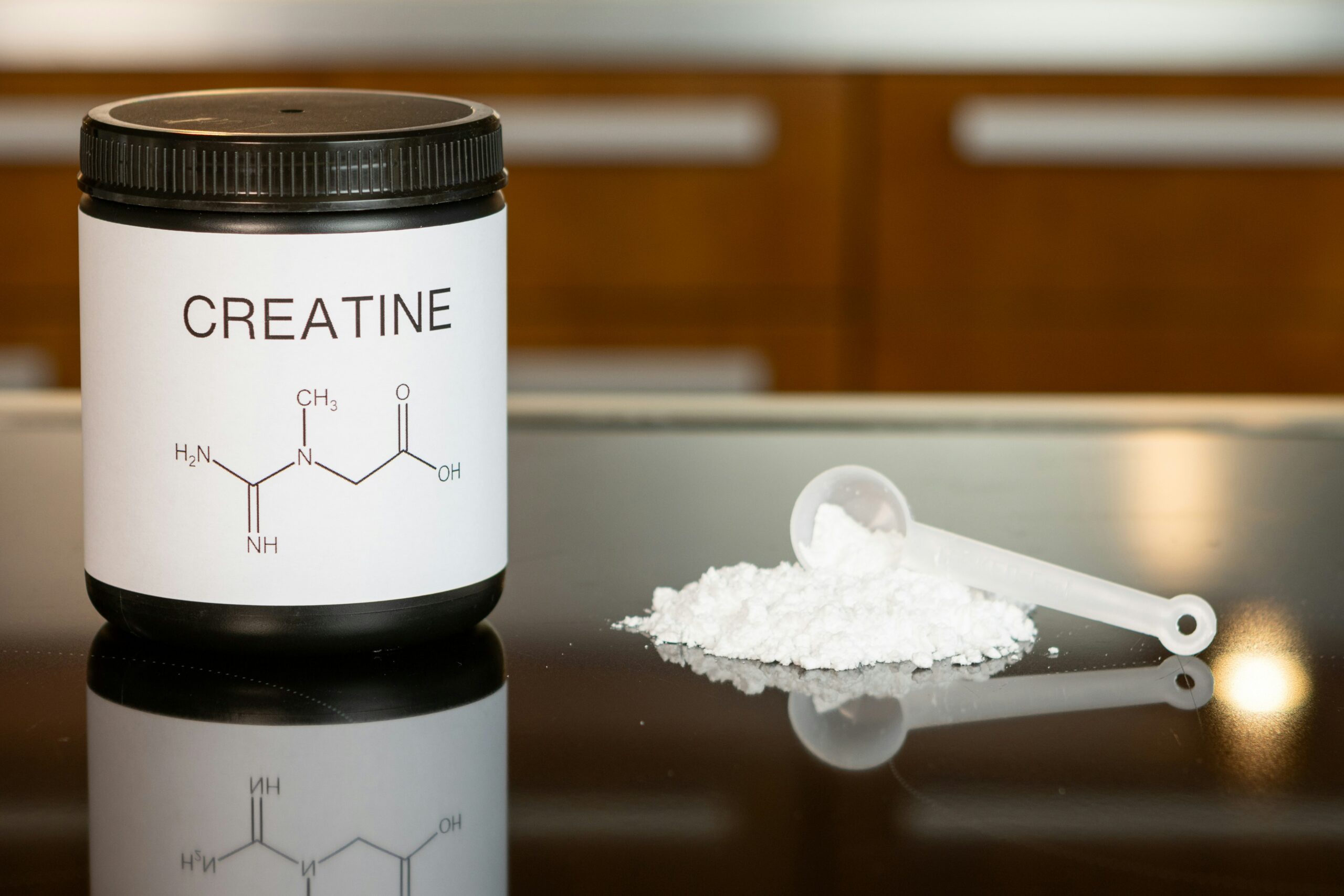 Pote de creatina monohidratada com fórmula química na embalagem e dosador com pó branco, demonstrando suplementação esportiva