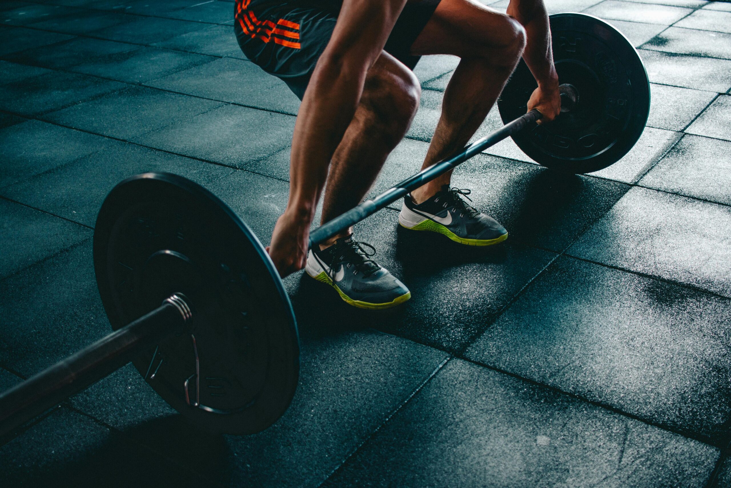 Atleta masculino realizando exercício de levantamento terra com barra olímpica e anilhas em academia com piso emborrachado