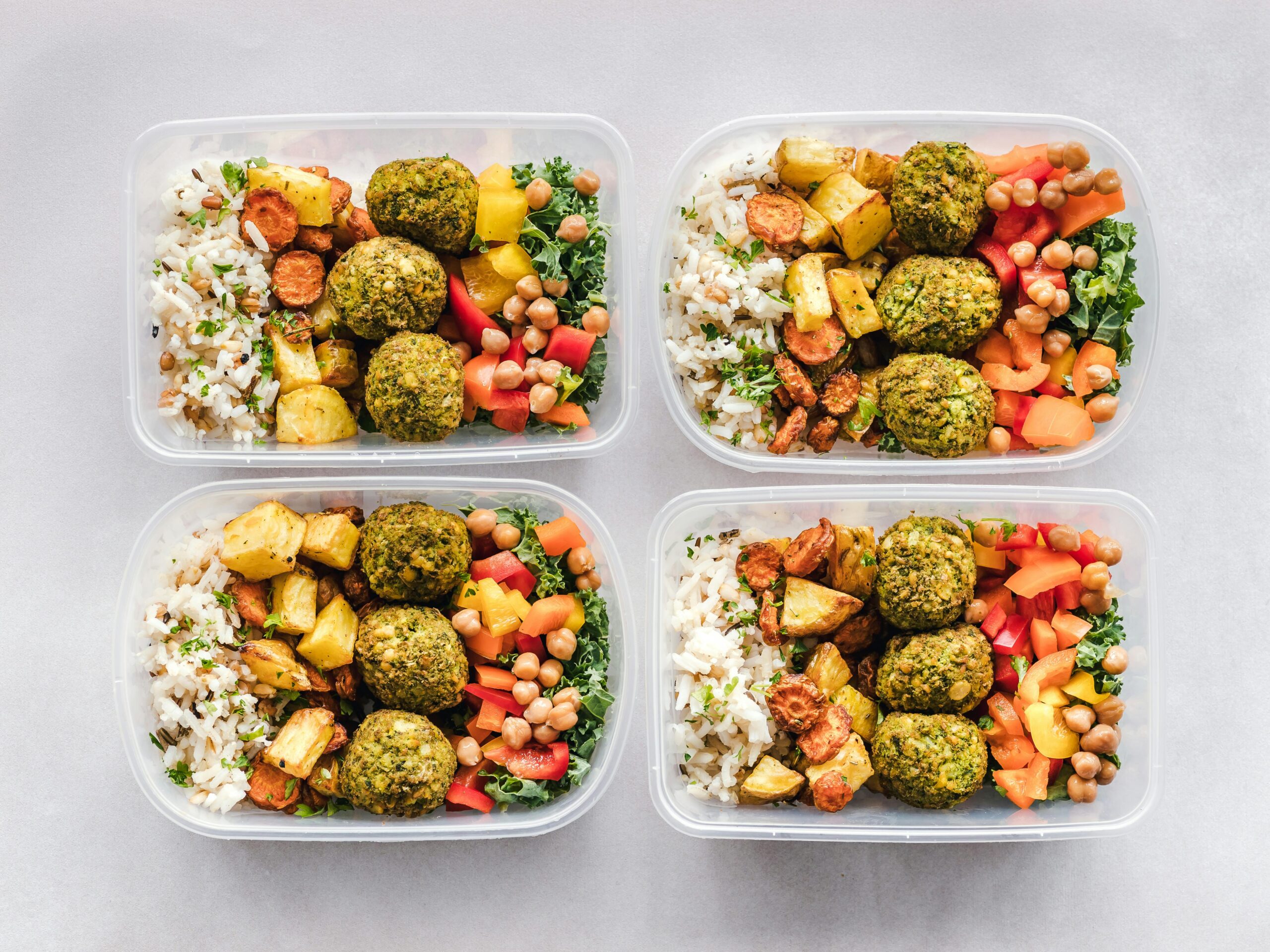Quatro marmitas preparadas com arroz integral, grão-de-bico, vegetais coloridos e almôndegas vegetais, representando refeições saudáveis e balanceadas para diferentes tipos de dieta