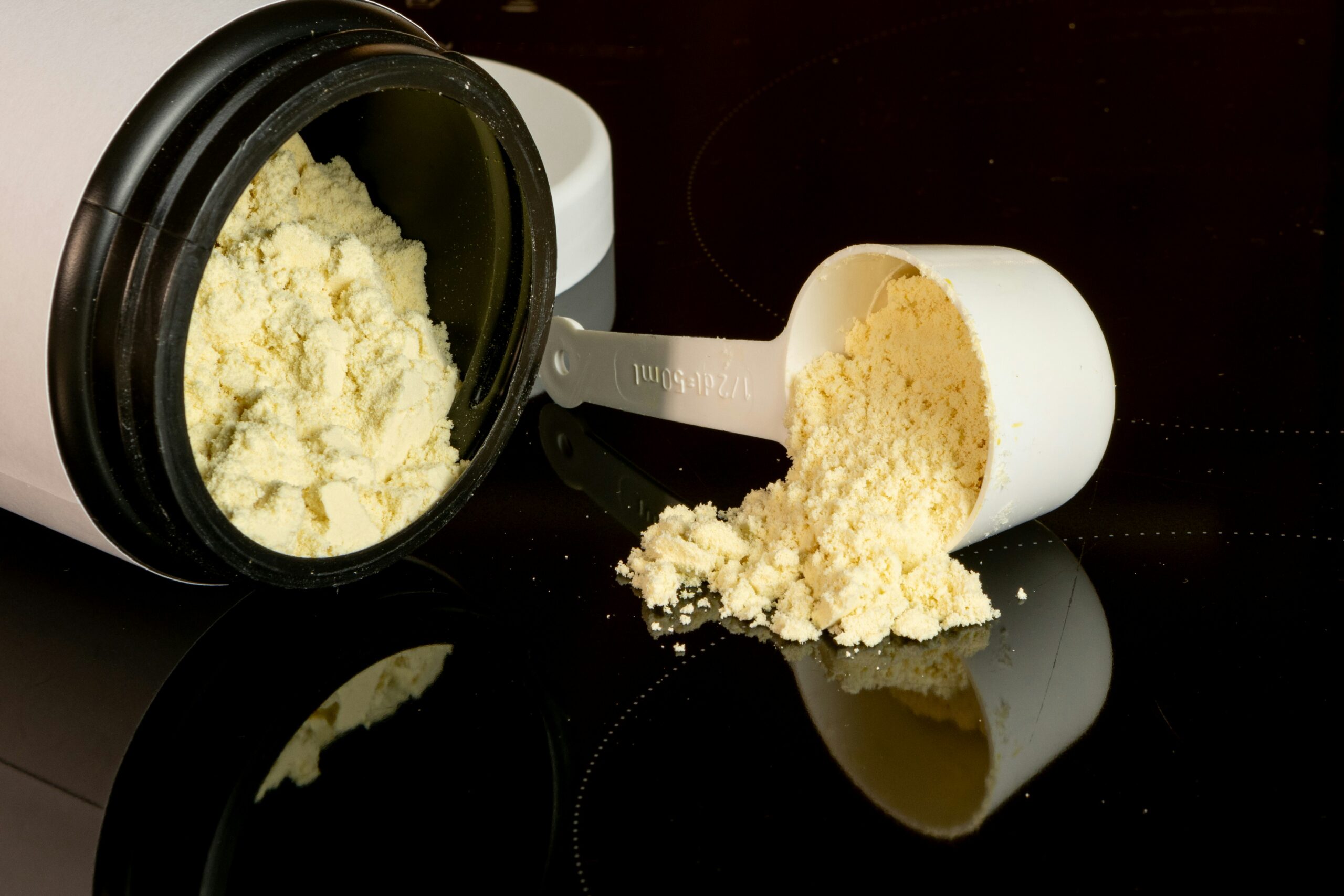 Pote de whey protein aberto com dosador medindo proteína em pó, mostrando textura e consistência do suplemento proteico