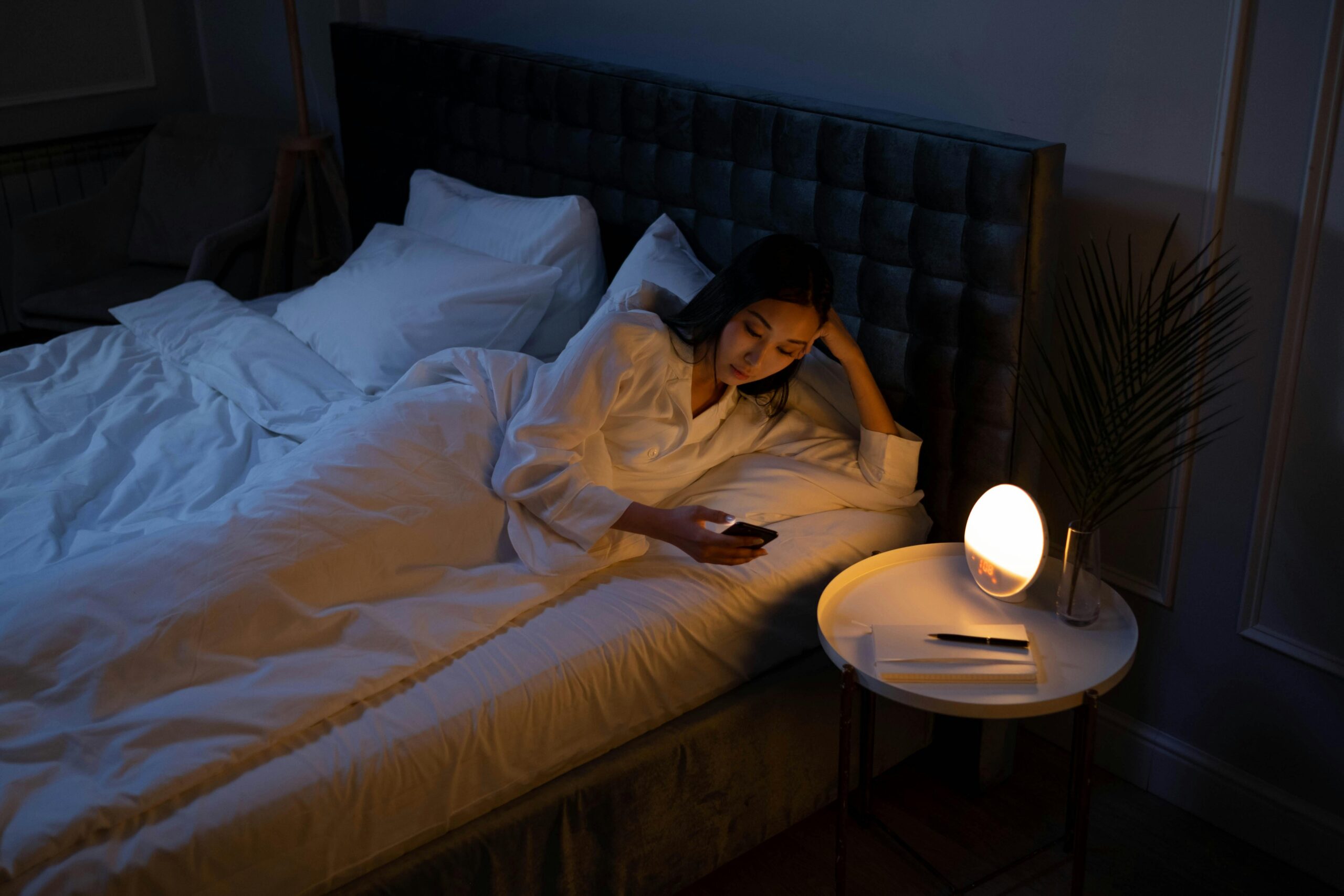Mulher deitada na cama usando smartphone à noite com luz artificial ambiente, demonstrando hábitos que prejudicam a qualidade do sono e podem causar ganho de peso