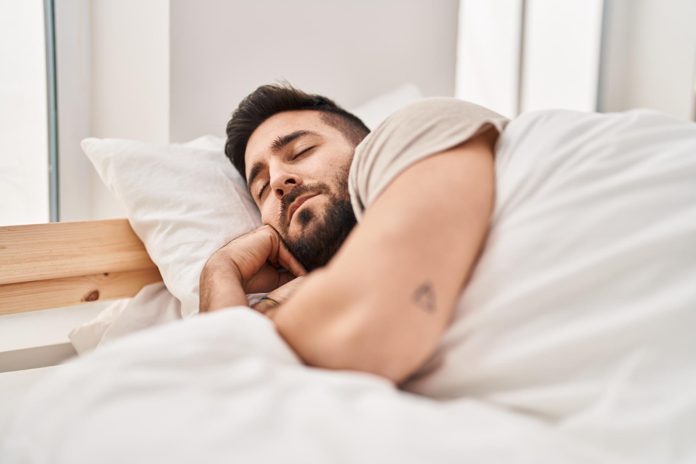 Homem barbudo dormindo tranquilamente em cama confortável com lençóis brancos em quarto com luz natural suave