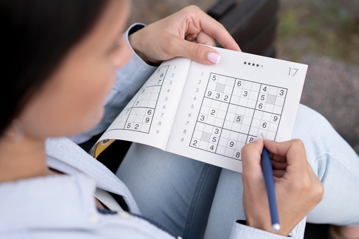 Mãos de pessoa concentrada resolvendo quebra-cabeças Sudoku em papel, representando exercícios mentais e benefícios cognitivos baseados em evidências científicas